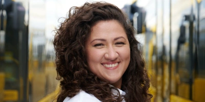 Auszubildende Havva steht in BVG-Arbeitskleidung zwischen zwei BVG-Bussen und schaut in die Kamera