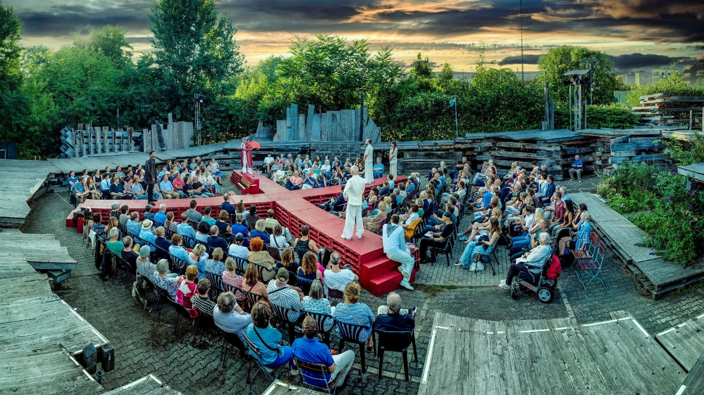 Aufnahme des Globe Berlin Theaters. bei dem unter freiem Himmel das Publikum zwischen Laufstegen sitzt. Auf diesen Laufstegen wird Theater gespielt.