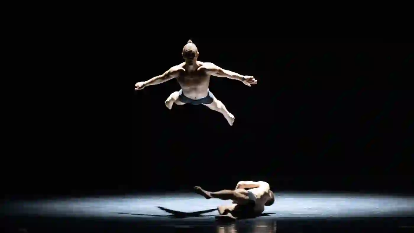 Zu sehen sind zwei Tänzer auf einer dunklen Bühne.